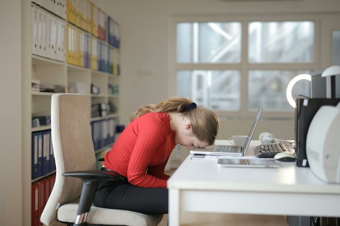 Woman in red sweater leaning on desk frustrated at office, illustrating wild stories from folks who quit their jobs quickly.