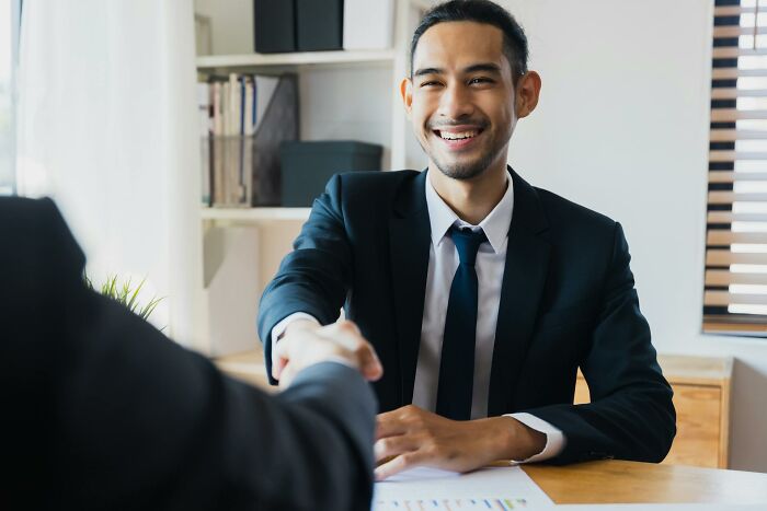 Young man in a suit smiling and shaking hands during an interview about quitting jobs in record time and why they left.
