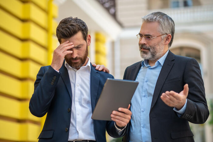 Two men in business suits discussing work while one looks stressed, illustrating stories of quitting jobs quickly.