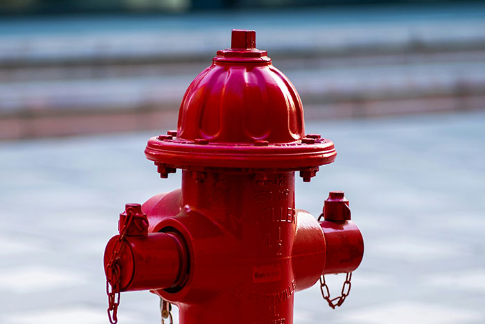 Bright red fire hydrant with two capped outlets and chains against a blurred urban background highlighting truly random facts.