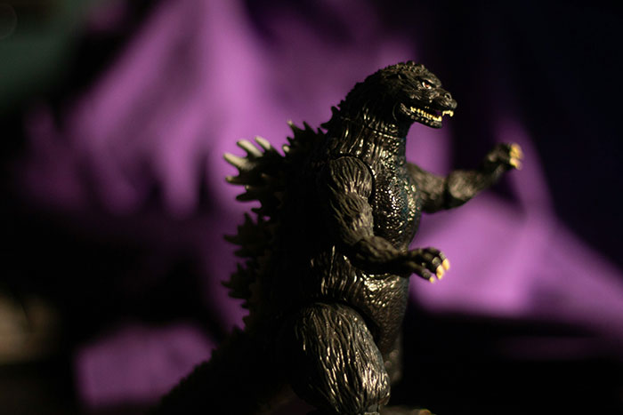 Black Godzilla figure with textured skin and sharp spines, posed against a blurred purple background, random facts theme.