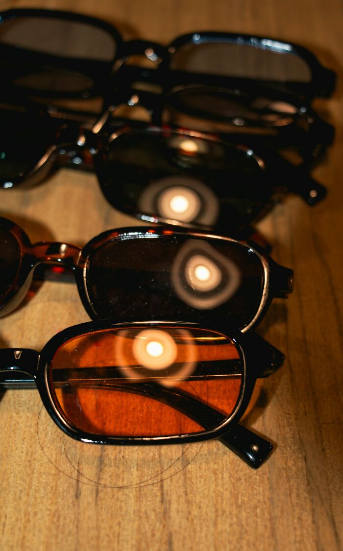 Several pairs of lost sunglasses with dark and amber lenses laid out on a wooden surface, owners never returned for them.