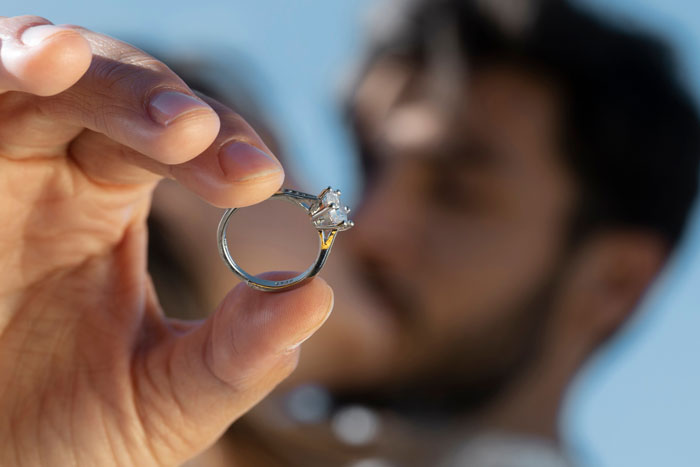 Close-up of a person holding a family heirloom ring, highlighting a diamond set in a silver band against a blurred background. Close-up of a person holding a family heirloom ring, highlighting a diamond set in a silver band against a blurred background.