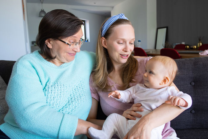 Older woman and mother smiling while holding and playing with baby granddaughter on a couch at home. Older woman and mother smiling while holding and playing with baby granddaughter on a couch at home.