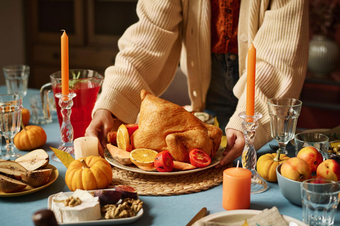 Woman cancels Thanksgiving, placing roasted turkey on decorated table with candles, pumpkins and autumn fruit