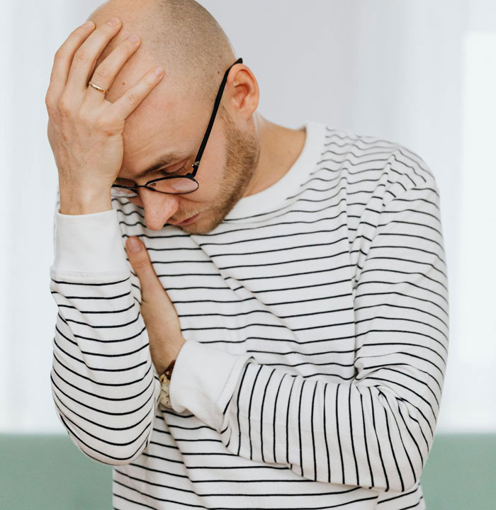 Man in striped shirt and glasses looking stressed while holding his head, illustrating picky eater dilemma at Christmas dinner. Man in striped shirt and glasses looking stressed while holding his head, illustrating picky eater dilemma at Christmas dinner.
