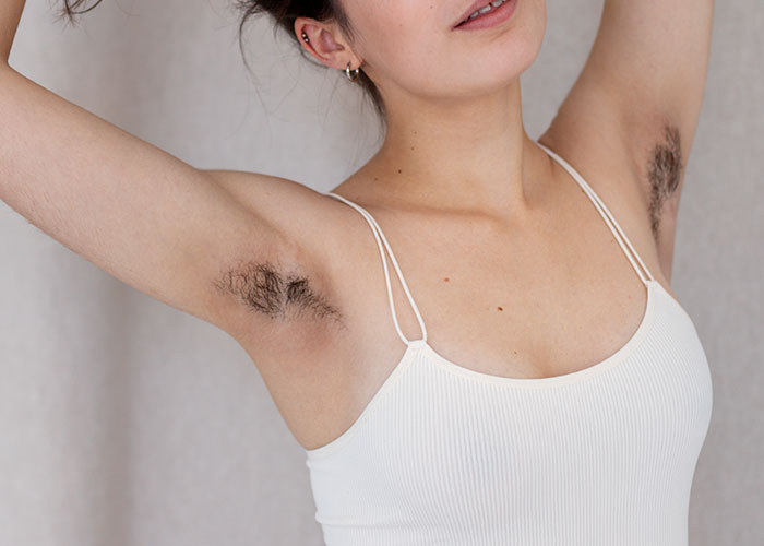 Woman showing hairy armpits in a white tank top, highlighting bridal guests feeling uncomfortable with body hair. Woman showing hairy armpits in a white tank top, highlighting bridal guests feeling uncomfortable with body hair.