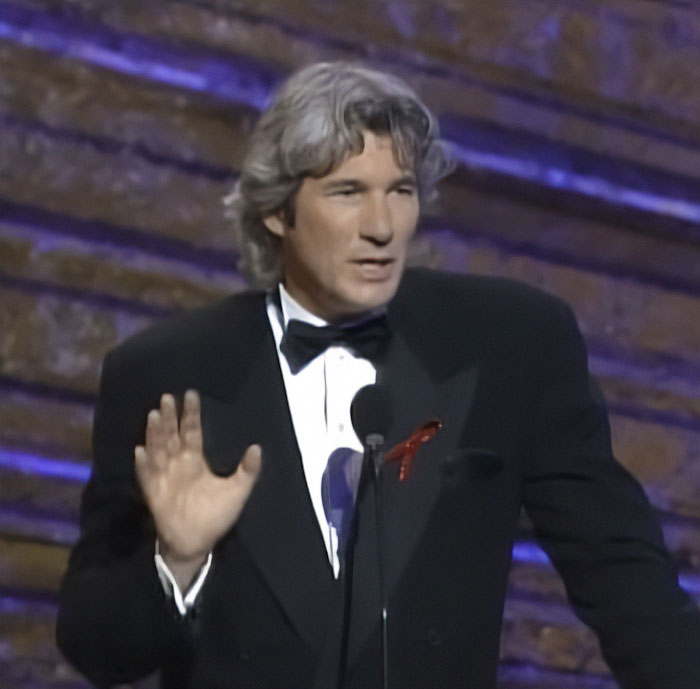 Richard Gere speaking at an event, wearing a black tuxedo and addressing the audience about Oscars ban controversy. Richard Gere speaking at an event, wearing a black tuxedo and addressing the audience about Oscars ban controversy.