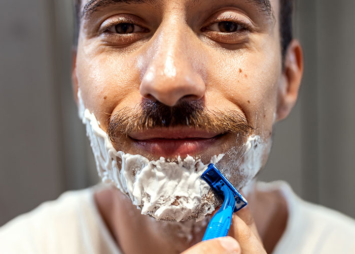 Close-up of a man shaving his face with a razor, highlighting online debates about the no makeup look preference. Close-up of a man shaving his face with a razor, highlighting online debates about the no makeup look preference.