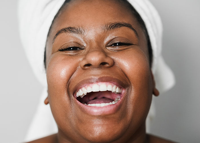 Close-up of a happy woman with glowing skin and towel wrapped on head, illustrating women online roasting men about no makeup look.