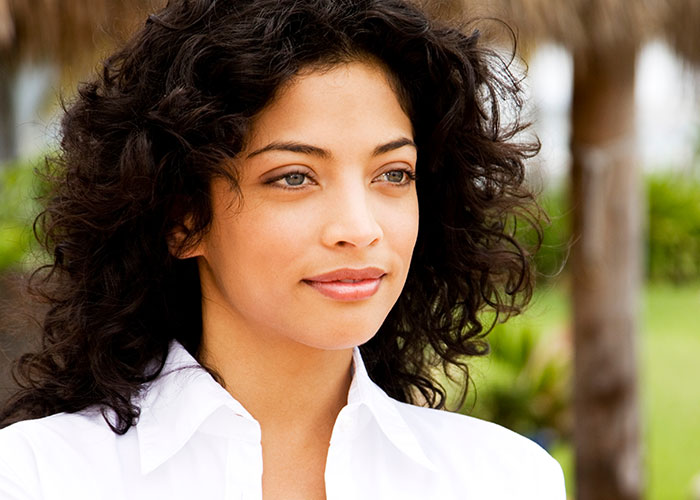 Young woman with curly hair in a white shirt, outdoors, illustrating women online roast men who prefer no makeup look.
