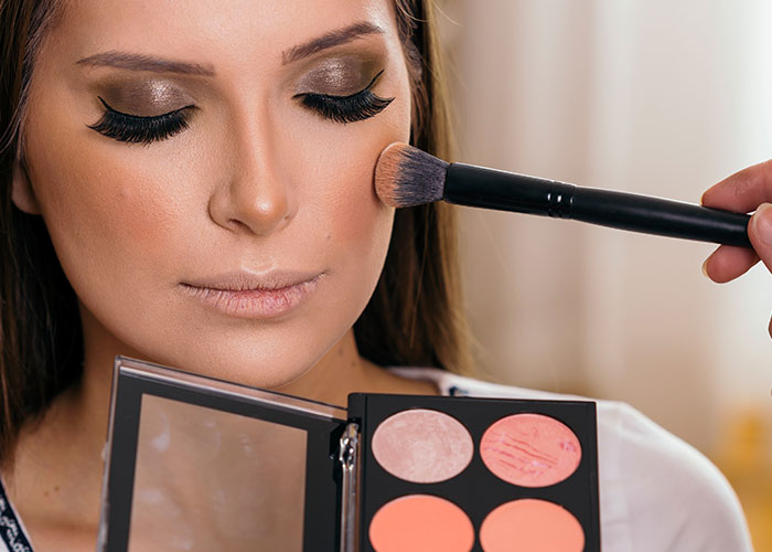 Woman having makeup applied with brush, showcasing bold eye makeup and blush from makeup palette close-up.