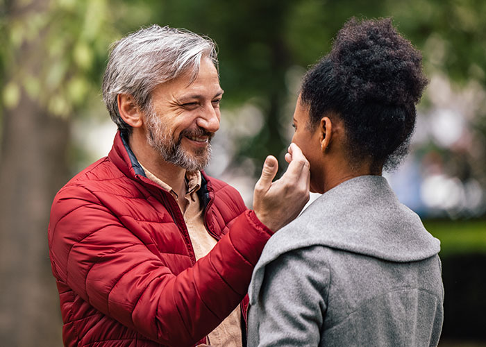 A man smiling and touching a woman’s face outdoors, illustrating women online roast men who prefer the no makeup look.