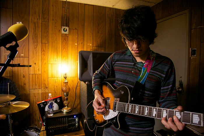 Young man playing electric guitar in a wood-paneled room, practicing music as an example of a once-famous regular job.