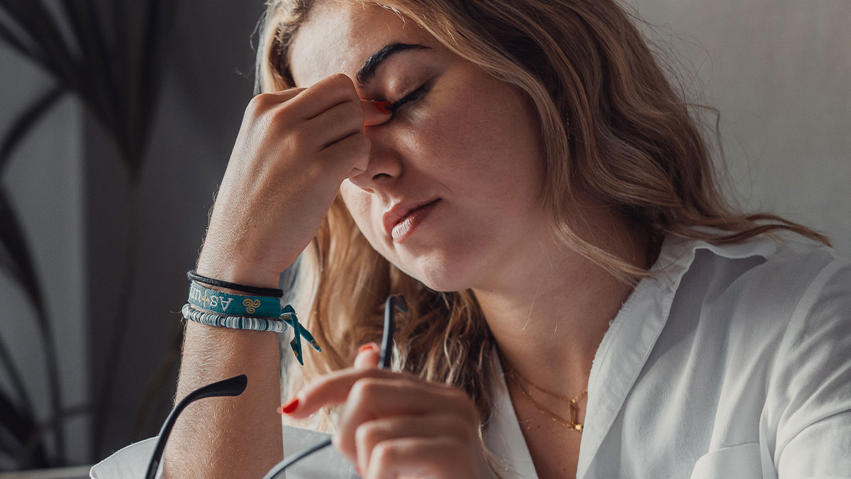Stressed woman in white shirt holding glasses, expressing frustration after women ruin MIL surprise by pretending ignorance.
