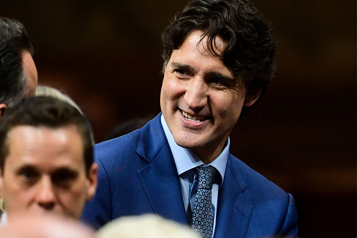 Justin Trudeau smiling in a blue suit and patterned tie during a public event with blurred people around him.
