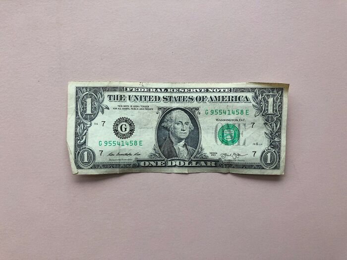One dollar bill lying flat on a light pink surface symbolizing secrets people trust strangers online with.