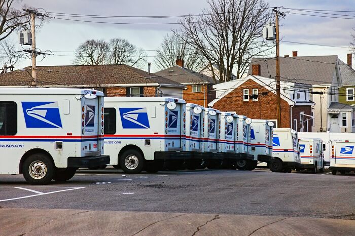 Line of USPS postal delivery trucks parked outside residential neighborhood on a clear day showing postal worker vehicles.