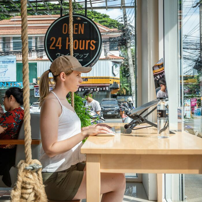 Young digital nomad working on a laptop in a cafe with a view of the street, illustrating remote work lifestyle.