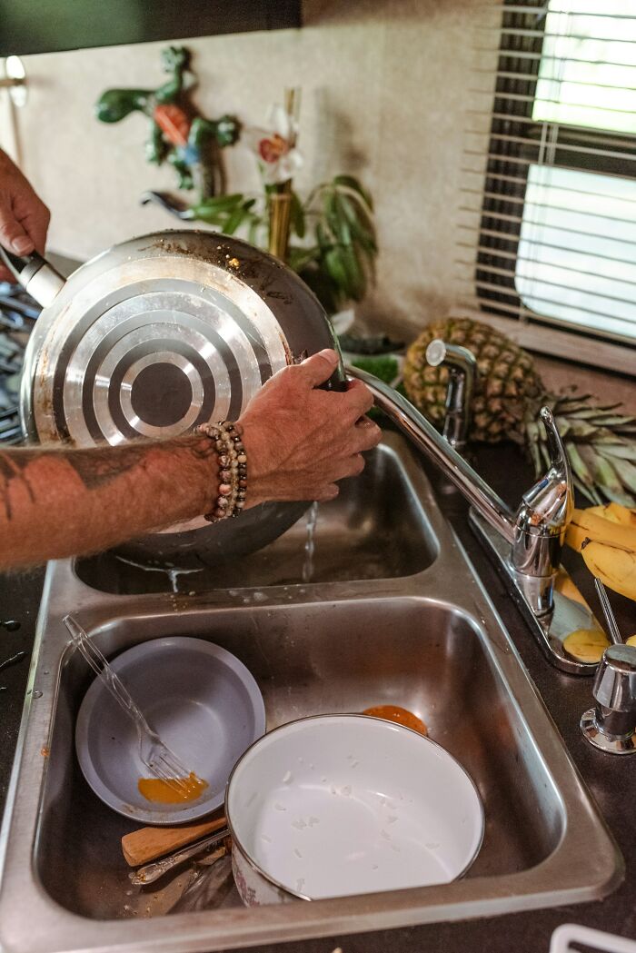 Person washing a snobbish attitude away while rinsing dishes in a kitchen sink with fruit nearby and natural light coming in.