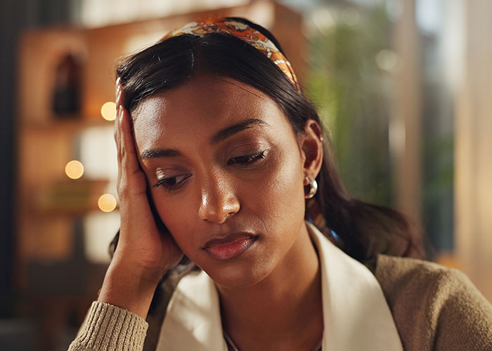 Young woman looking distressed and worried, sitting indoors, depicting the feeling of being held hostage at parents’ place. Young woman looking distressed and worried, sitting indoors, depicting the feeling of being held hostage at parents’ place.