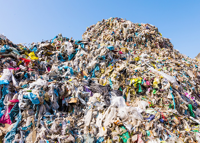 Large pile of mixed plastic waste under clear sky representing microplastics pollution affecting bone tissue studies.