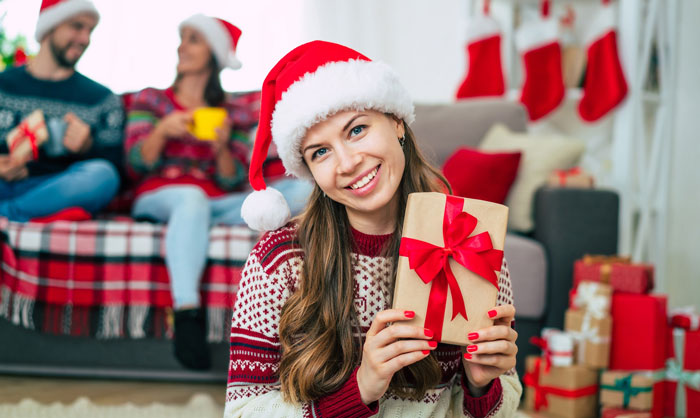 Woman in Santa hat holding a gift, smiling during a family Secret Santa with a festive holiday background.