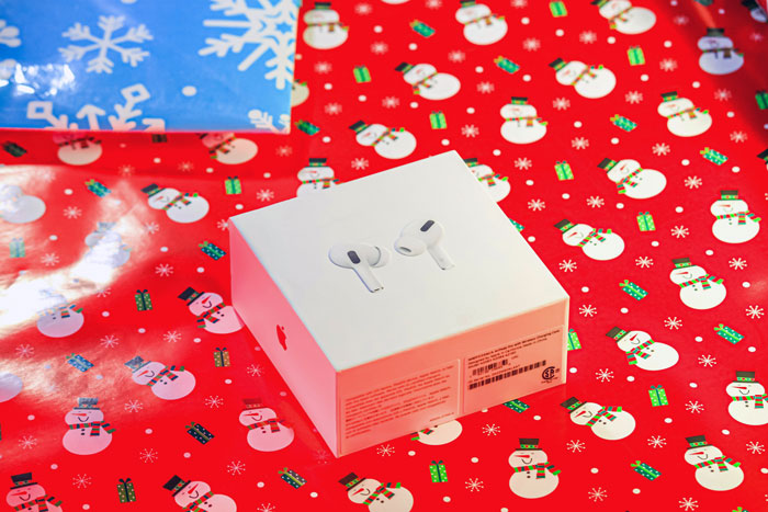 Apple AirPods Pro box on festive wrapping paper, illustrating a luxe shopping list in family Secret Santa gift exchange. Apple AirPods Pro box on festive wrapping paper, illustrating a luxe shopping list in family Secret Santa gift exchange.