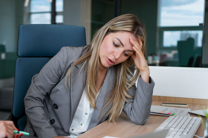 Woman looking conflicted at her desk in an office setting after a coworker told her to stay home and birth babies.