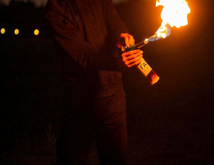 Person holding a canister with flames shooting out, illustrating a crazy airport story involving fire or danger.