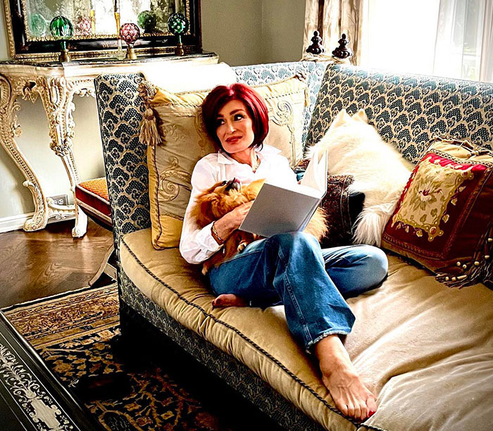 Kris Jenner sitting barefoot on a vintage sofa reading a book, showing hands without gloves after viral facelift news. Kris Jenner sitting barefoot on a vintage sofa reading a book, showing hands without gloves after viral facelift news.