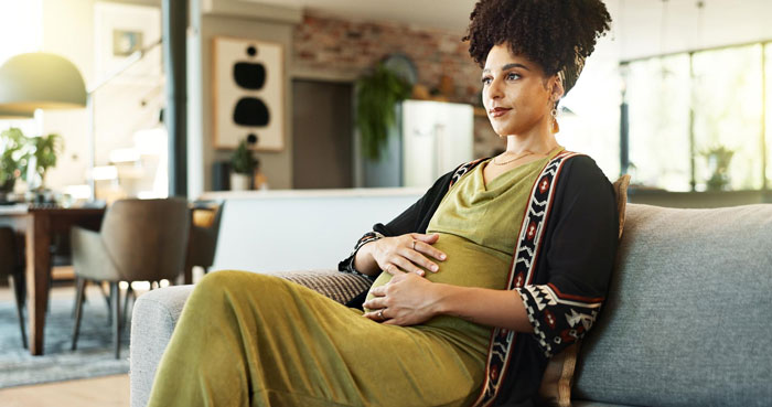 Pregnant woman sitting on couch at home, reflecting on complicated feelings about adoption and race issues. Pregnant woman sitting on couch at home, reflecting on complicated feelings about adoption and race issues.
