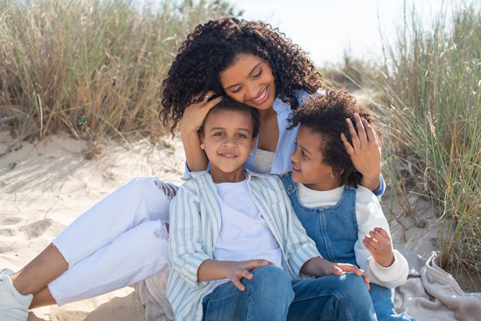 Woman with two mixed race children sitting outdoors on sand, reflecting on friend wanting white baby adoption conflict. Woman with two mixed race children sitting outdoors on sand, reflecting on friend wanting white baby adoption conflict.