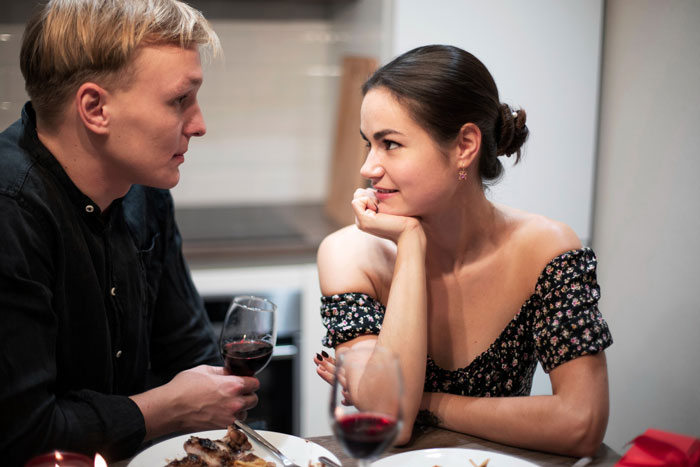 Man and woman having a serious conversation over dinner, man holding wine glass, woman smiling and listening intently.