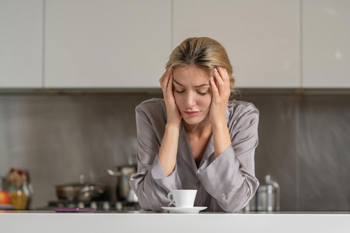 Young woman looking distressed and holding her head in a modern kitchen, reflecting on relationship issues.