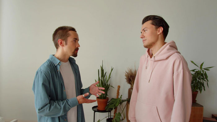 Two young men arguing indoors surrounded by potted plants, illustrating boys will be boys entitled behavior conflict. Two young men arguing indoors surrounded by potted plants, illustrating boys will be boys entitled behavior conflict.