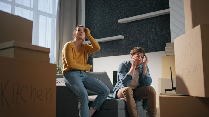 Frustrated woman and man sitting amid moving boxes labeled kitchen and living room in a tense household scene. Frustrated woman and man sitting amid moving boxes labeled kitchen and living room in a tense household scene.