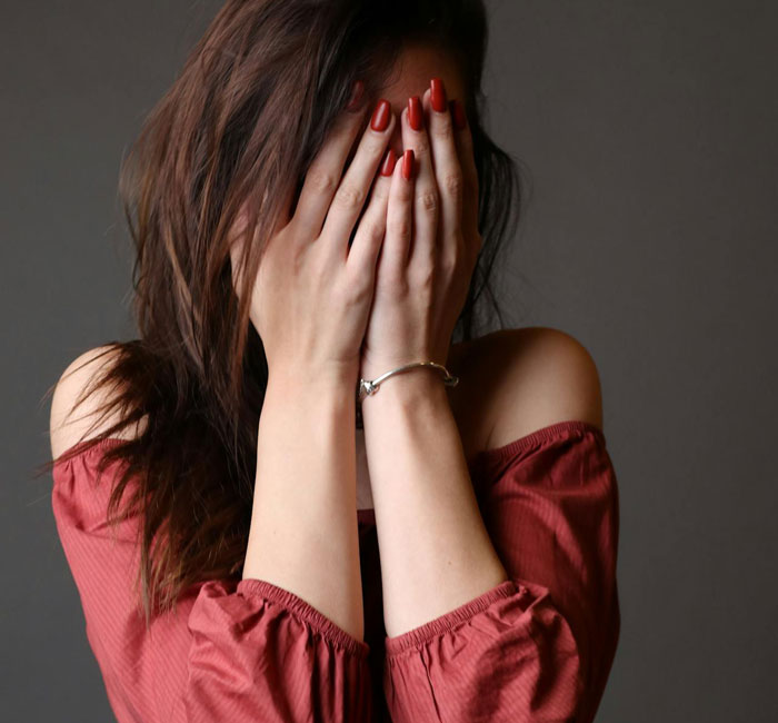 Woman in a red off-shoulder top covering her face, depicting emotional reaction to barefoot spiritual advisor chaos at Thanksgiving.