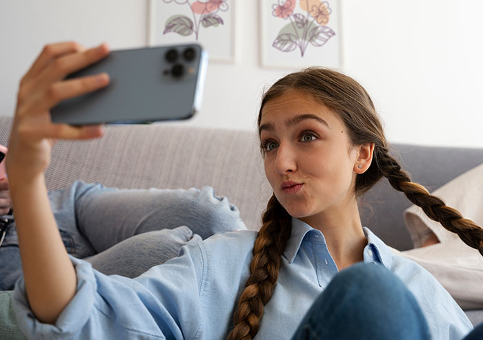 Young woman taking a selfie on smartphone, upset over sister building TikTok fame by lying about her in family setting. Young woman taking a selfie on smartphone, upset over sister building TikTok fame by lying about her in family setting.