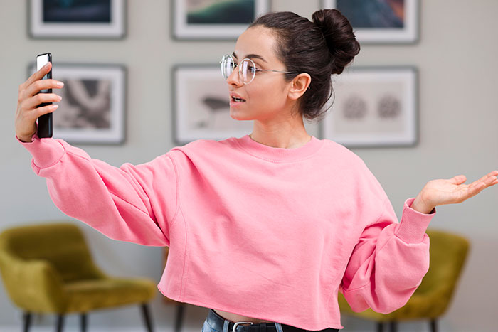 Woman in pink sweatshirt taking a selfie, upset about sister building TikTok fame by lying about her. Woman in pink sweatshirt taking a selfie, upset about sister building TikTok fame by lying about her.