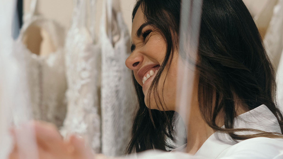Smiling woman looking at wedding dresses, saving her dress from jealous sister before wedding day conflict.
