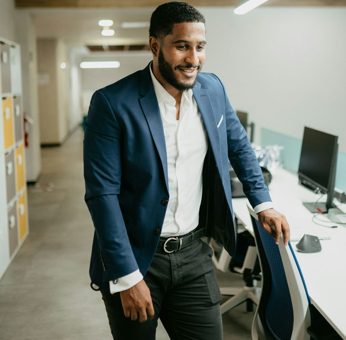Young Black man in business attire standing confidently in an office, showcasing a transformative new look trend.