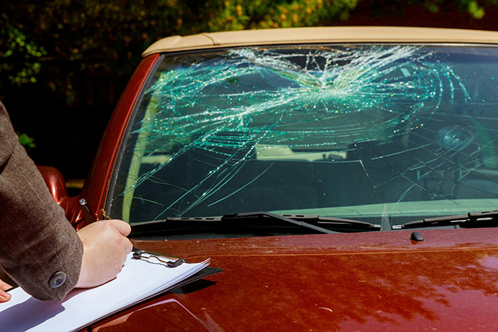 Person inspecting and taking notes on a car with a very c*****d windshield, highlighting wily criminals' clever tactics.