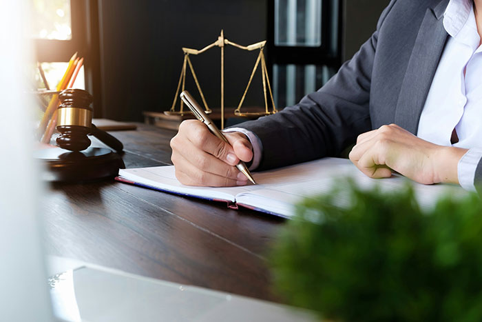 Person in suit writing in a notebook at desk with legal scales and gavel representing wily criminals outsmarting police officers.
