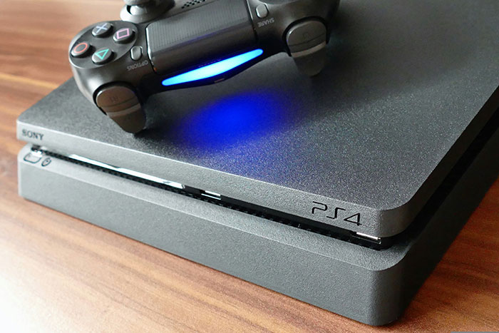 Sony PS4 gaming console with a controller glowing blue light on a wooden surface, highlighting clever gadget design.