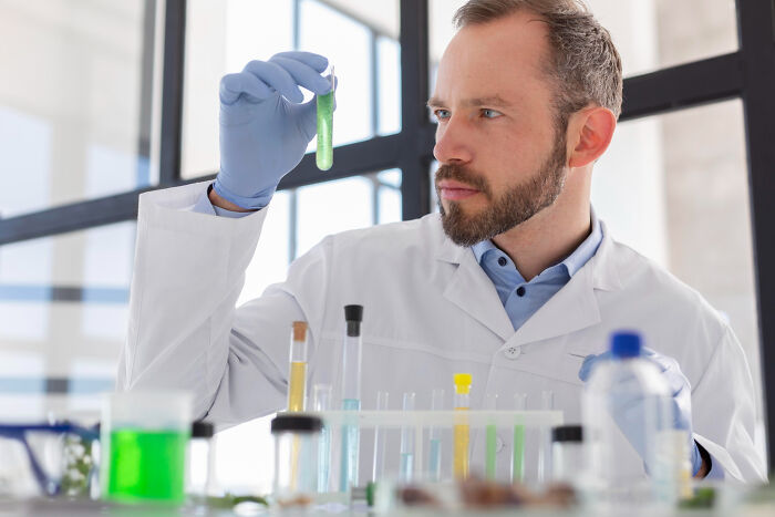 Male scientist in a lab coat examining a test tube, representing the concept of most likely to succeed and plot twists.