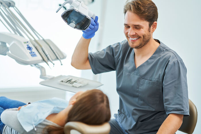 Male dentist smiling and preparing a dental light for a young patient during a routine checkup in a bright clinic.