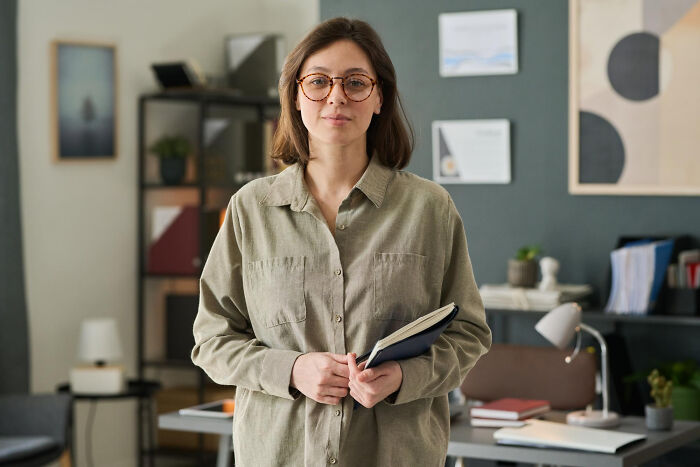 Young woman holding a notebook in a modern office, representing stories of people most likely to succeed with unexpected twists.