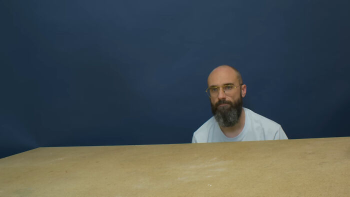 Bearded man with glasses sitting behind a table against a blue background, reflecting on most likely to succeed stories.