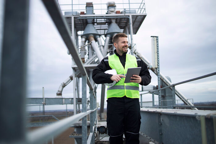 Man wearing safety vest and holding a tablet on industrial site, illustrating people who were most likely to succeed stories.